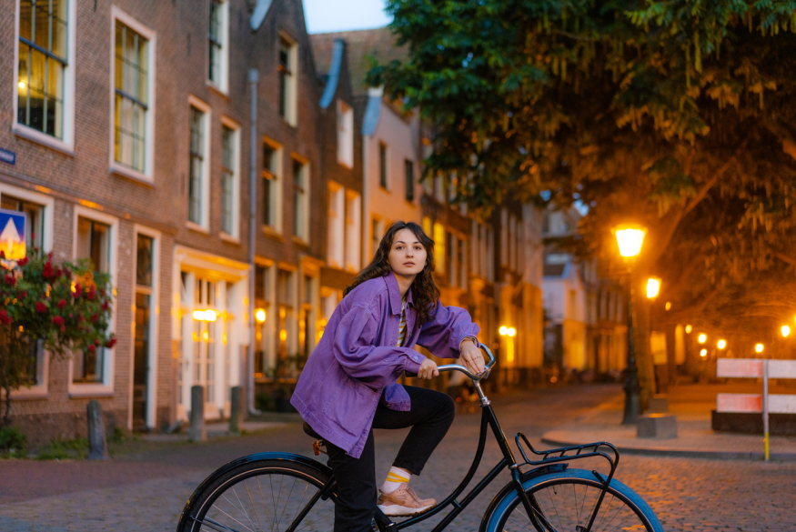 Leerling met paarse jas op de fiets in de stad in de schemering
