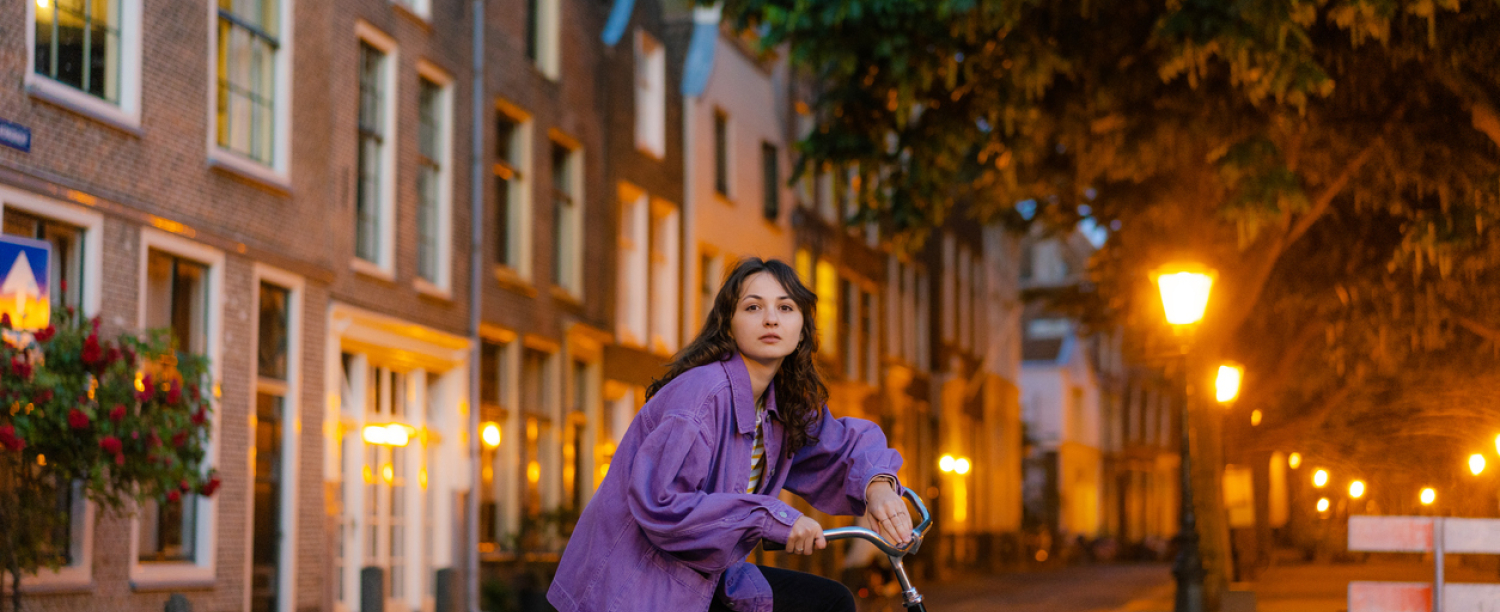 Leerling met paarse jas op de fiets in de stad in de schemering